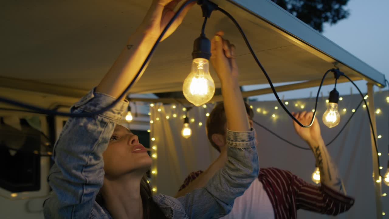 pareja joven haciendo decoraciones de luces en el coche camper por la noche