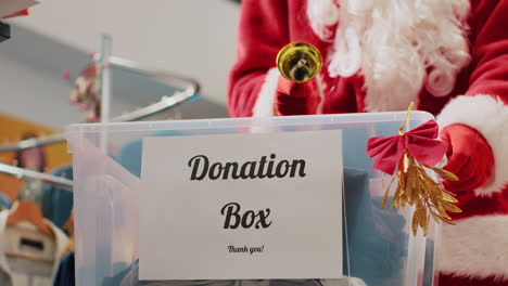 close up shot of donation box in fashion shop set up for humanitarian help during christmas holiday season. worker dressed as santa claus collecting unneeded clothes from generous clients