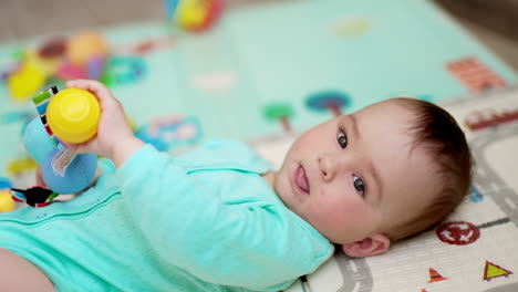 little cute lying on back showing tongue to the camera. adorable toddler holding a toy in his hands. close up. blurred backdrop.