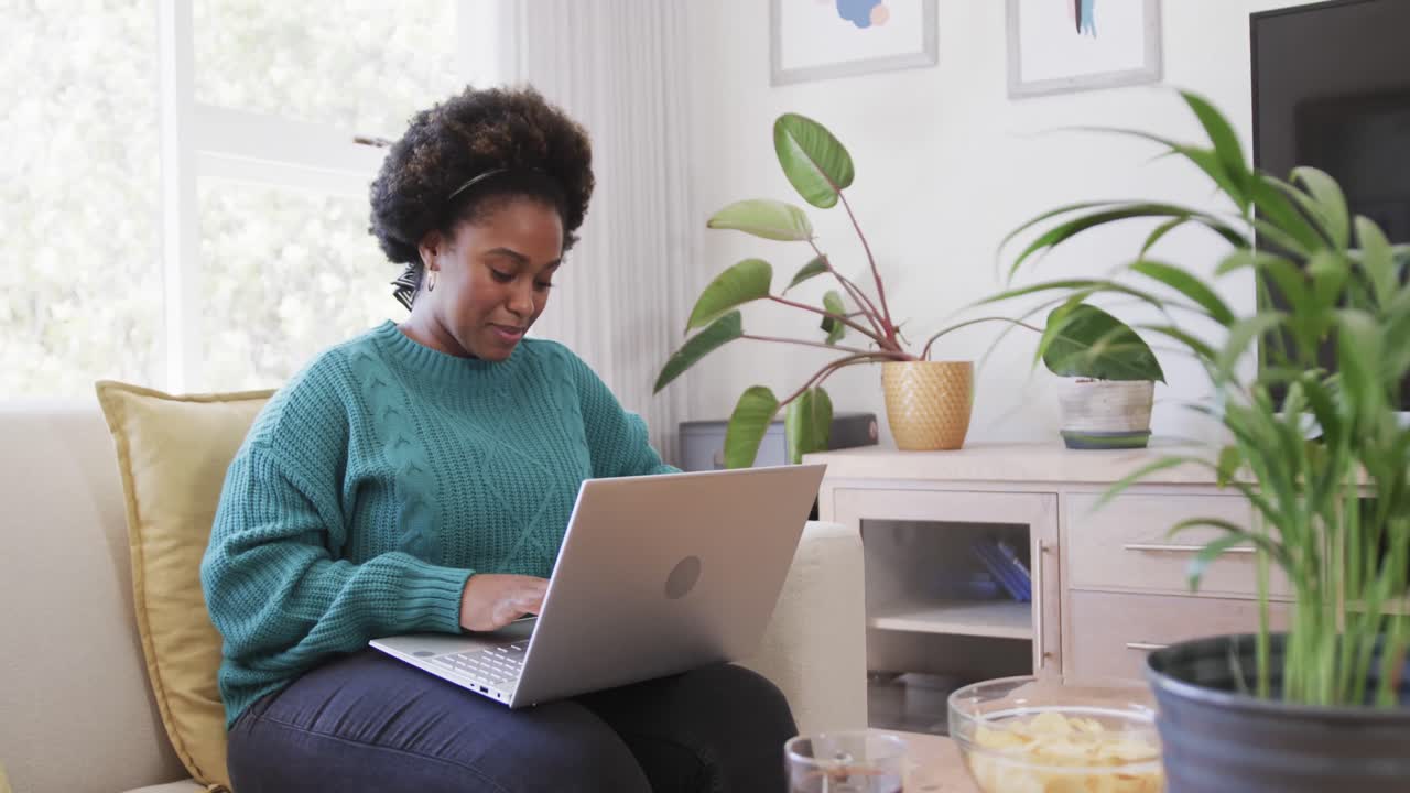 Portrait of happy african american woman sitting on couch using laptop at home, slow motion