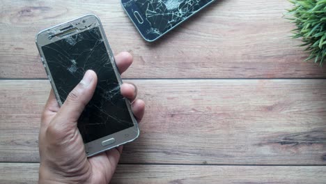 a hand holding a broken phone with a cracked screen.