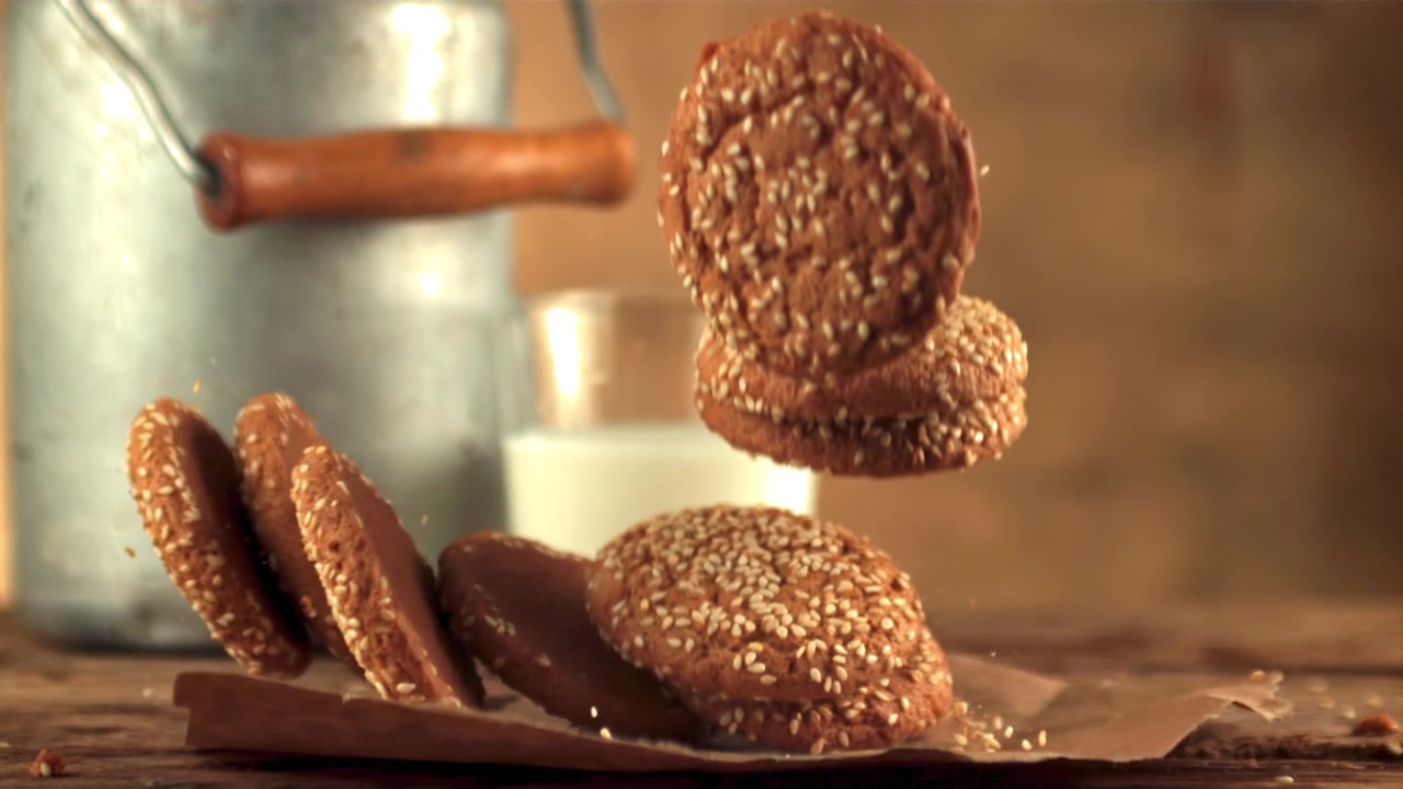 Slow Motion of Sesame Cookies Falling Next to a Glass of Milk