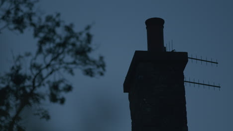 brick chimney silhouette with blurred tree branch and dark blue sky, static