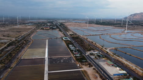 Panoramic-view-of-salt-fields-around-Phan-rang,-road-and-wind-turbines