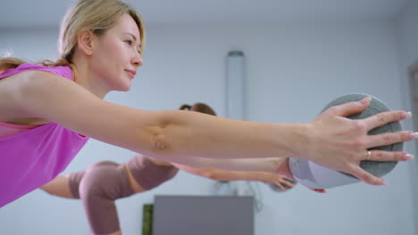 two women engaged in a fitness exercise holding foam rollers in a modern, urban-style room with minimalistic decor, the workout emphasizes balance, coordination, and strength training