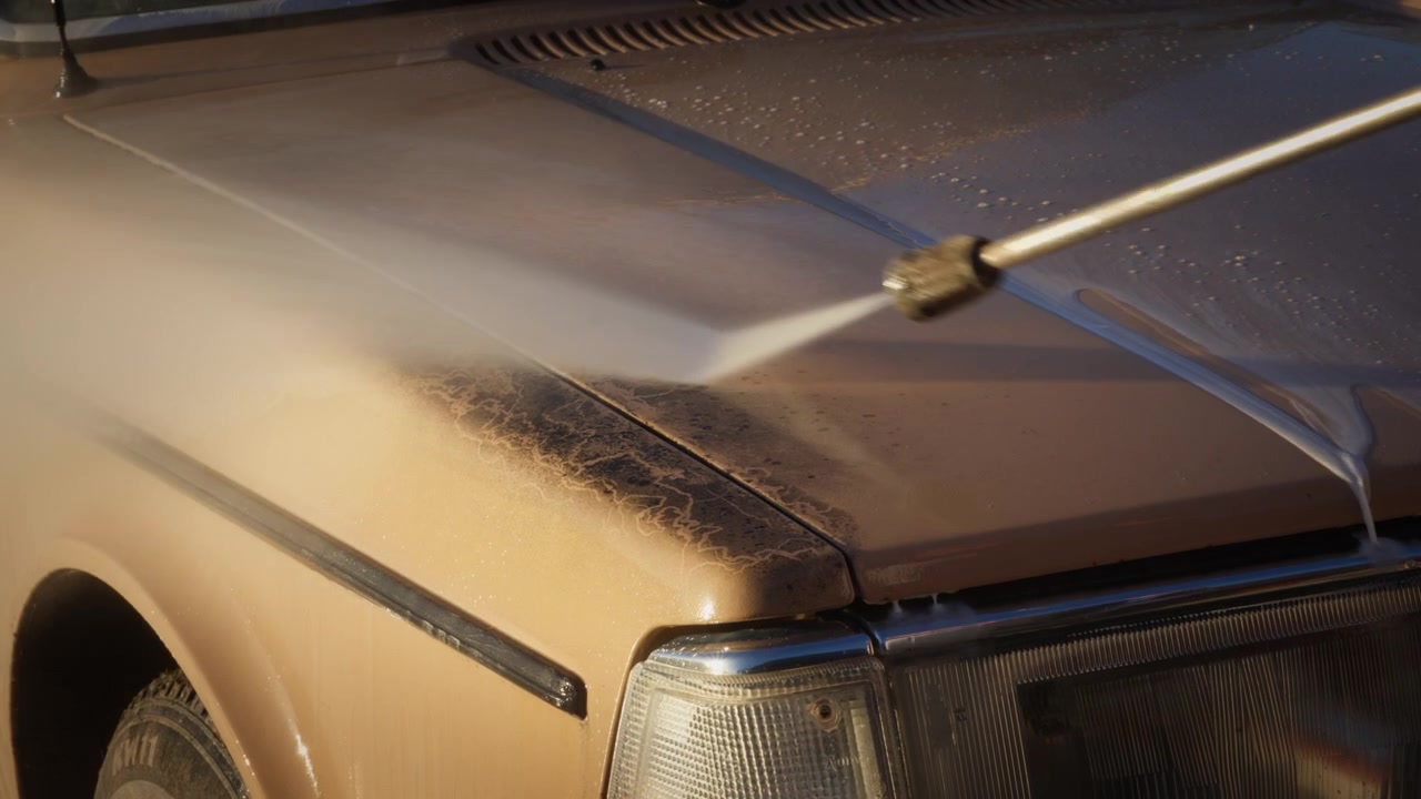 Primo piano di un'auto d'epoca abbandonata che viene pulita con un'idropulitrice. L'acqua rimuove lo sporco dal cofano, ideale per il restauro di auto, il detailing e contenuti su veicoli d'epoca