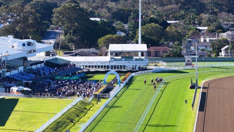 Drone captures horses and jockeys beginning a race on a green turf track at an Australian racecourse, with bright daylight and clear visibility
