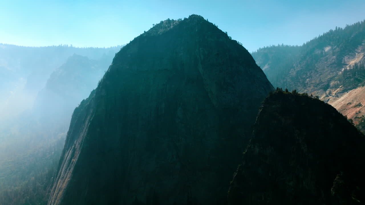 Two high rocks with some trees growing on top. Beautiful mountains in the fog in Yosemite National Park, United States.