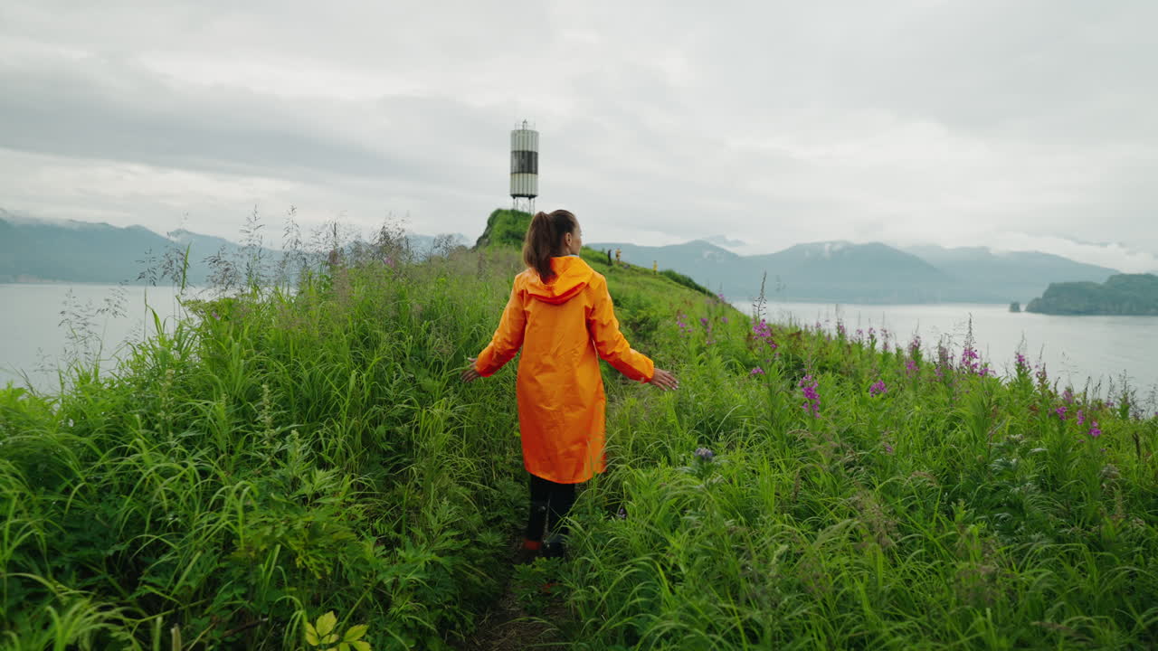 Woman in an Orange Raincoat Hiking on a Coastal Path
