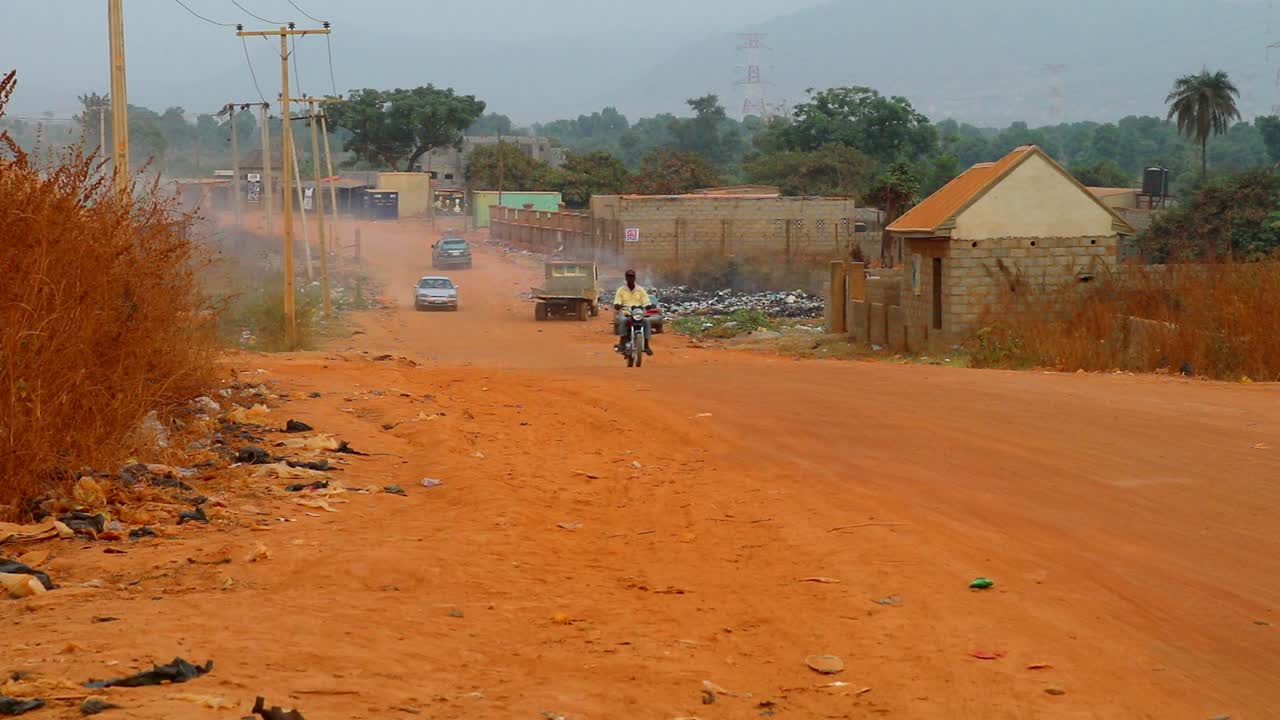 Motorists and bikers ride uphill on a dusty African air polluted road.