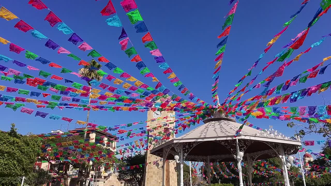town square decorated with colorful flags with its kiosk and bell tower in Mexico