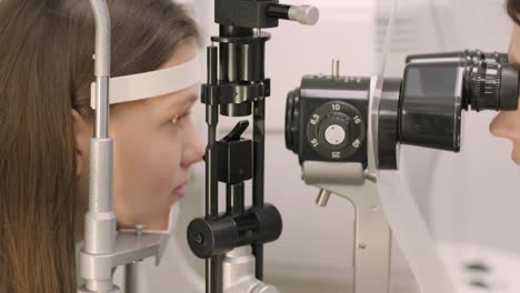 ophthalmologist check eyesight of young teen with modern equipment. doctor checking eyes with biomicroscope device. dolly shot of female doctor examining eye structure with help of medical equipment