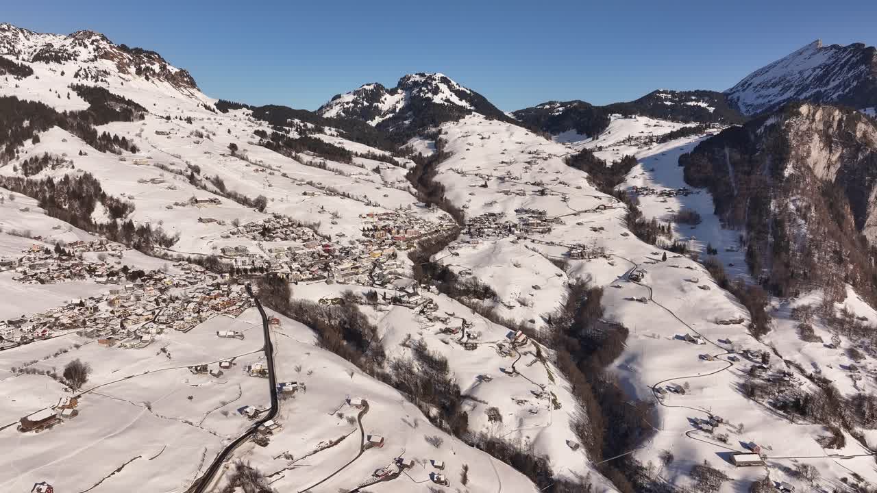 Aerial drone view of snow-covered village of Amden in Swiss alps, scenic mountain terrain, winding roads and serene winter landscapes of Walensee and Glarus region.