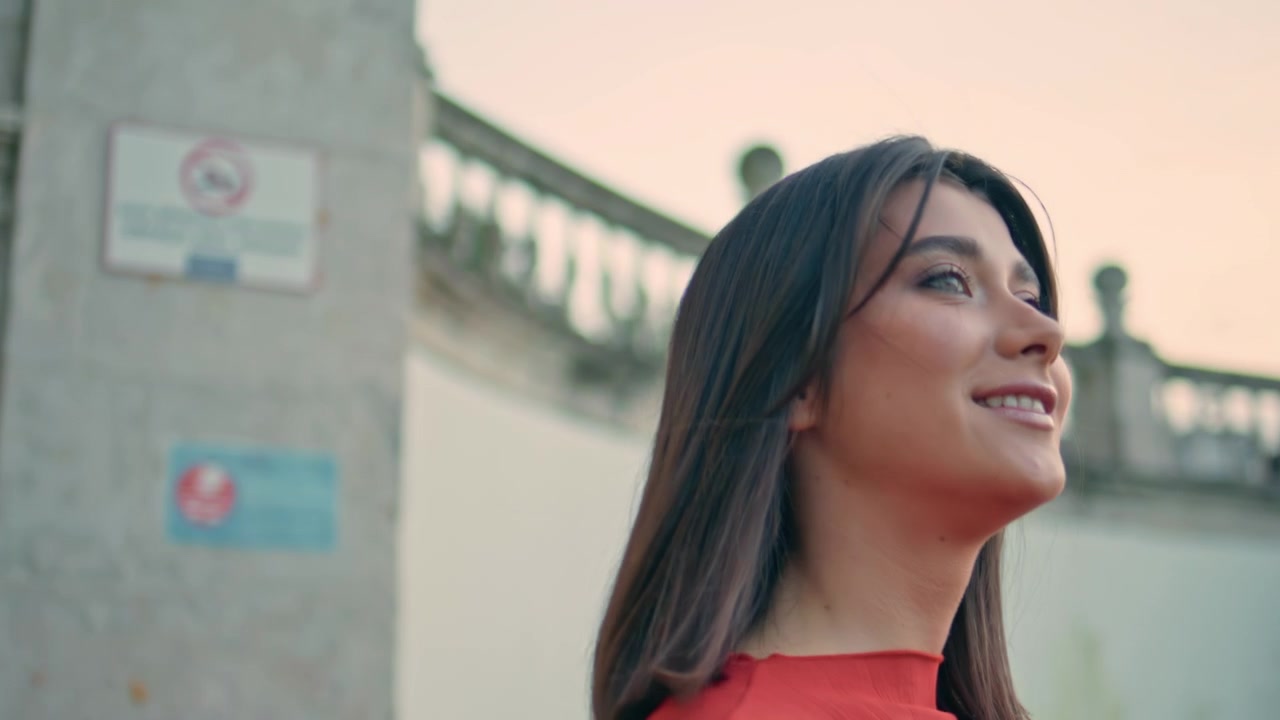 Brunette lady red dress turning back city stairs. Smiling girl looking up sky.