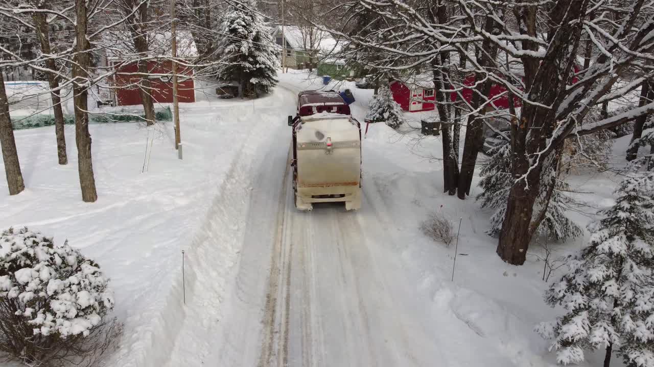 Sherbrooke, Canada, snowy road drone follows garbage truck driving during light storm