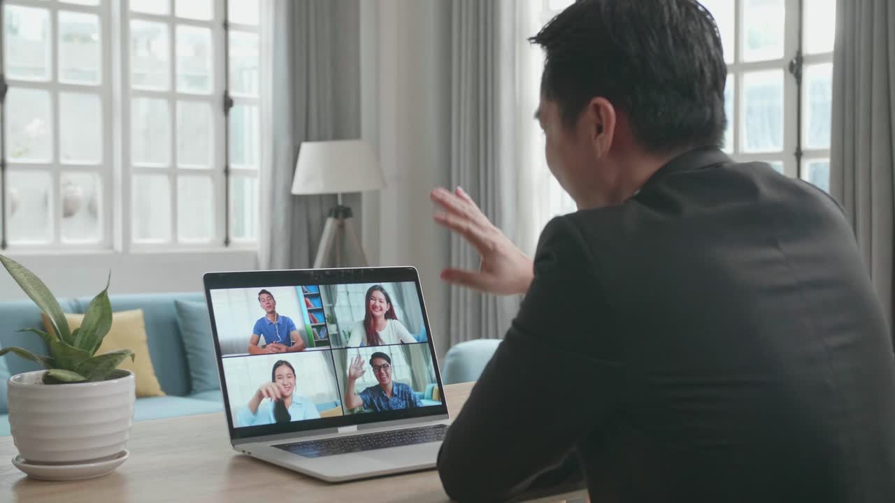 ビジネススーツを着たアジア人ビジネスマンが自宅で働いている間コンピューターで同僚とビデオコールをしている