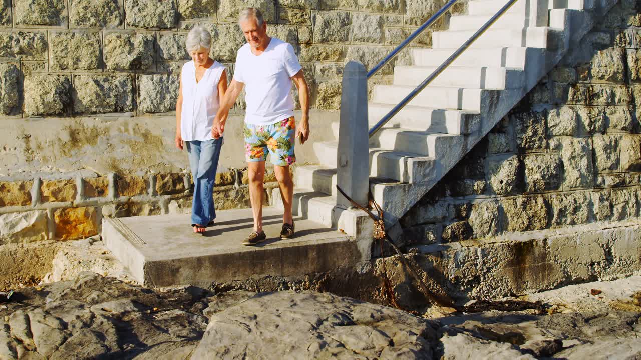 una pareja de ancianos caminando por las escaleras cerca de la playa 4k