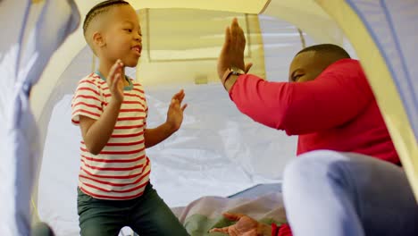 happy african american father and son having fun and high fiving in tent in garden, in slow motion