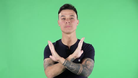 retrato de un joven guapo mirando a la cámara está estrictamente gesticulando con las manos cruzadas haciendo forma de x que significa negación diciendo no. pantalla verde