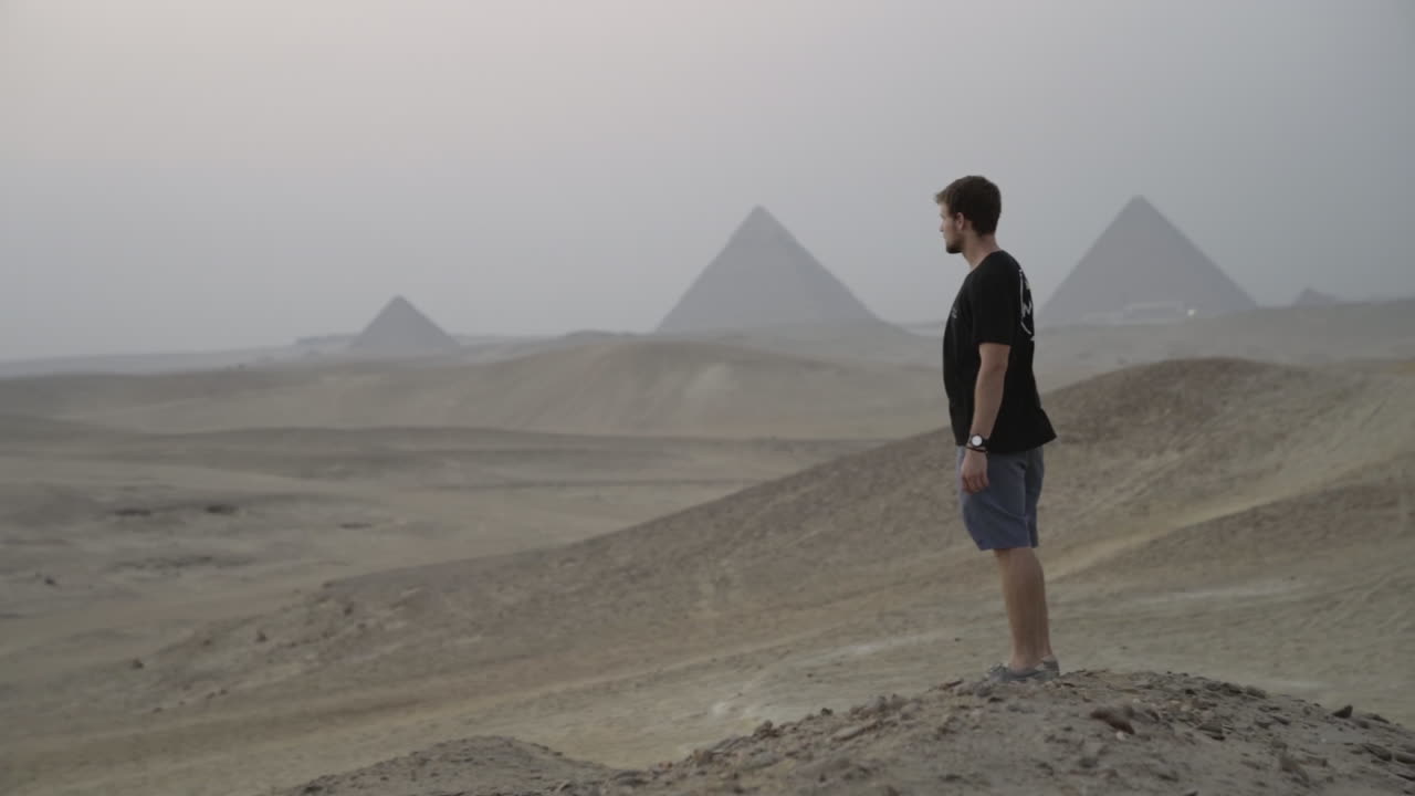 Young man looks out into desert while Giza Pyramids loom in background