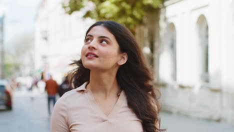 Portrait-of-Indian-woman-tourist-walking-in-urban-city-street,-smiling-having-positive-good-mood