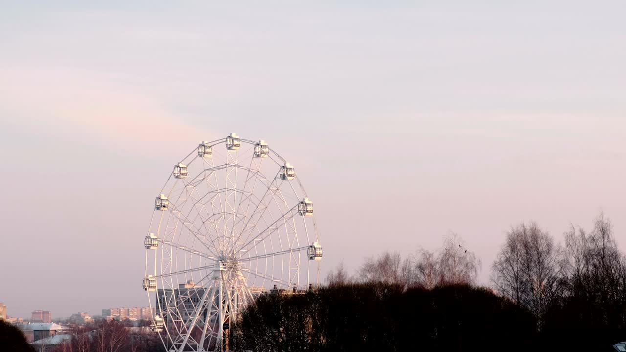 la rueda de ferris en el parque de invierno en el fondo de la ciudad. cielo rosado al atardecer.