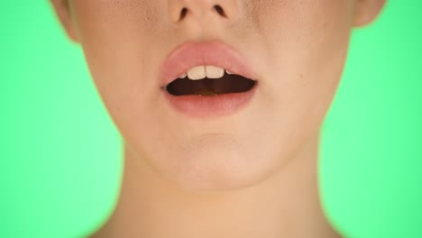 static close up shot of a young woman melting a delicious honey flavored candy on her tongue and sticking out her tongue against green background