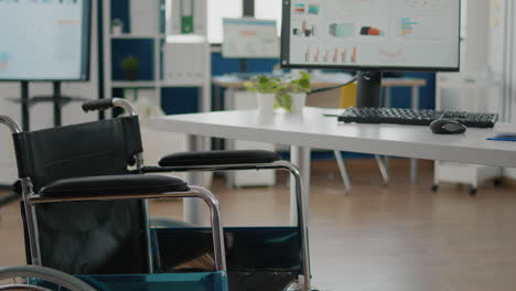 Wheelchair-parked-in-empty-office-room-near-desk-in-start-up-company