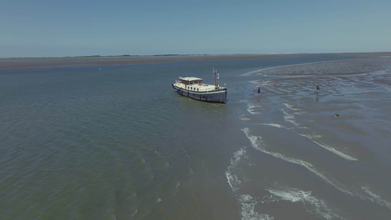 Traditional vessel resting on a tidal mudflat at low tide; smooth lateral tracking in neutral light. Wadden Sea
