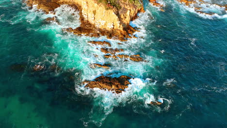 beautiful white foamy waves on the azure water hit the bare rocks lit with sunlight. top view on the shore of the pacific ocean.