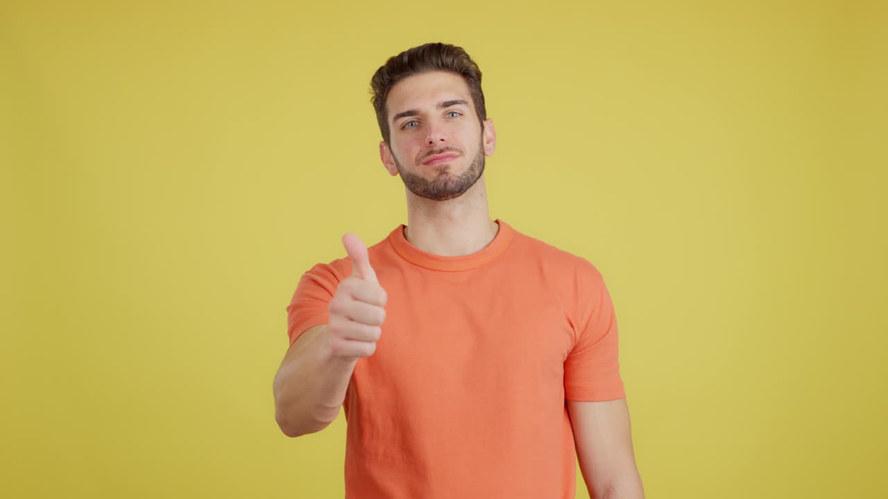 Young man giving a thumbs-up gesture against a yellow background