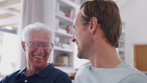 father with adult son talking on sofa at home together