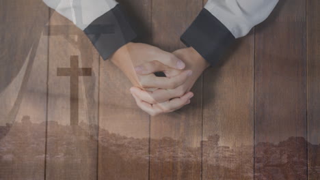 praying hands over cross and landscape animation on wooden background