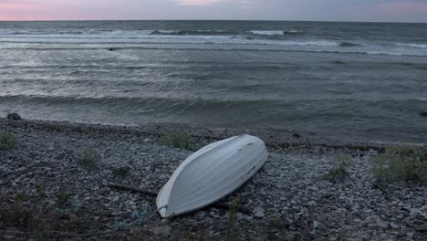 olas rompiendo en una playa rocosa en el mar báltico, un pequeño barco blanco se da la vuelta sobre su lado