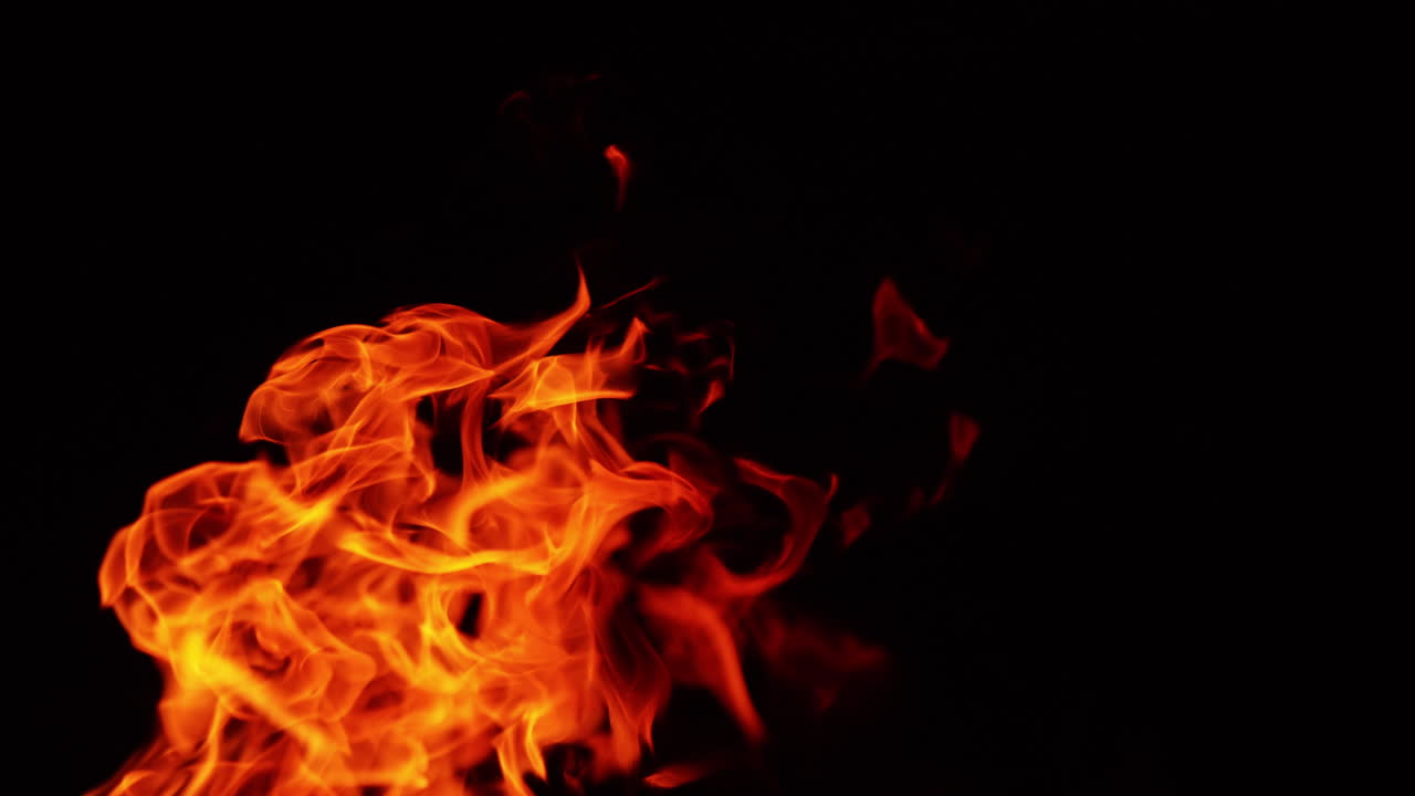 Red hot fire flames twirling in the darkness. Tiny sparkles flying up to the air. Close up.