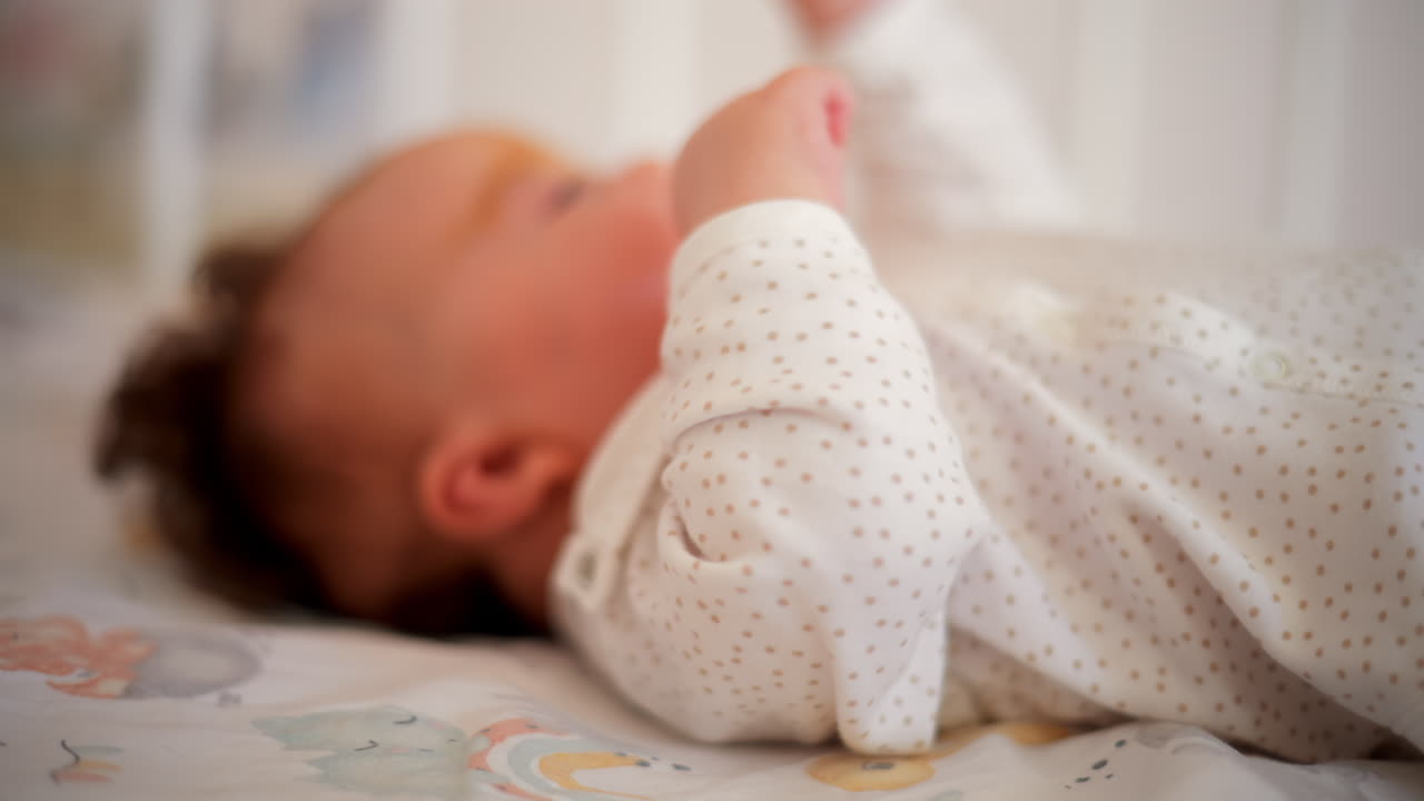 Un neonato in vestiti morbidi si muove delicatamente in una culla, allungando le piccole mani nella luce naturale del mattino