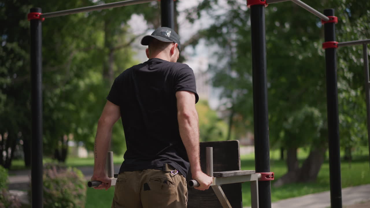 White Man Performing Tricep Dips Outdoors With Controlled Tempo And Focused Upper Body Engagement, Leafy Park Environment, Casual Cargo Pants And Cap, Deliberate Repetition And Grip