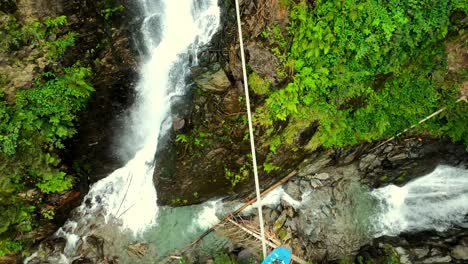 pov shot of a men with blue boots balancing very careful across a wild river and a waterfall on a steel cable bridge