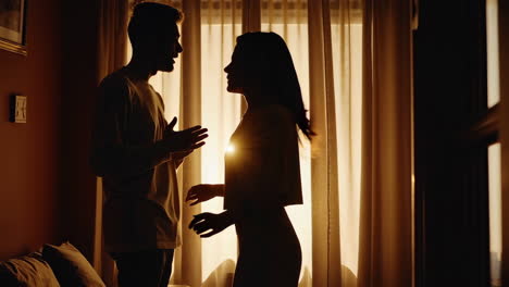 silhouetted couple discussing indoors by window