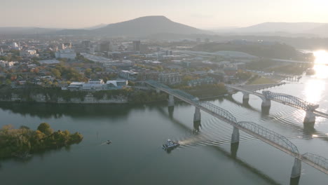 wide aerial footage of the tennessee river with downtown chattanooga and lookout mountain in the background and boats under the bridges