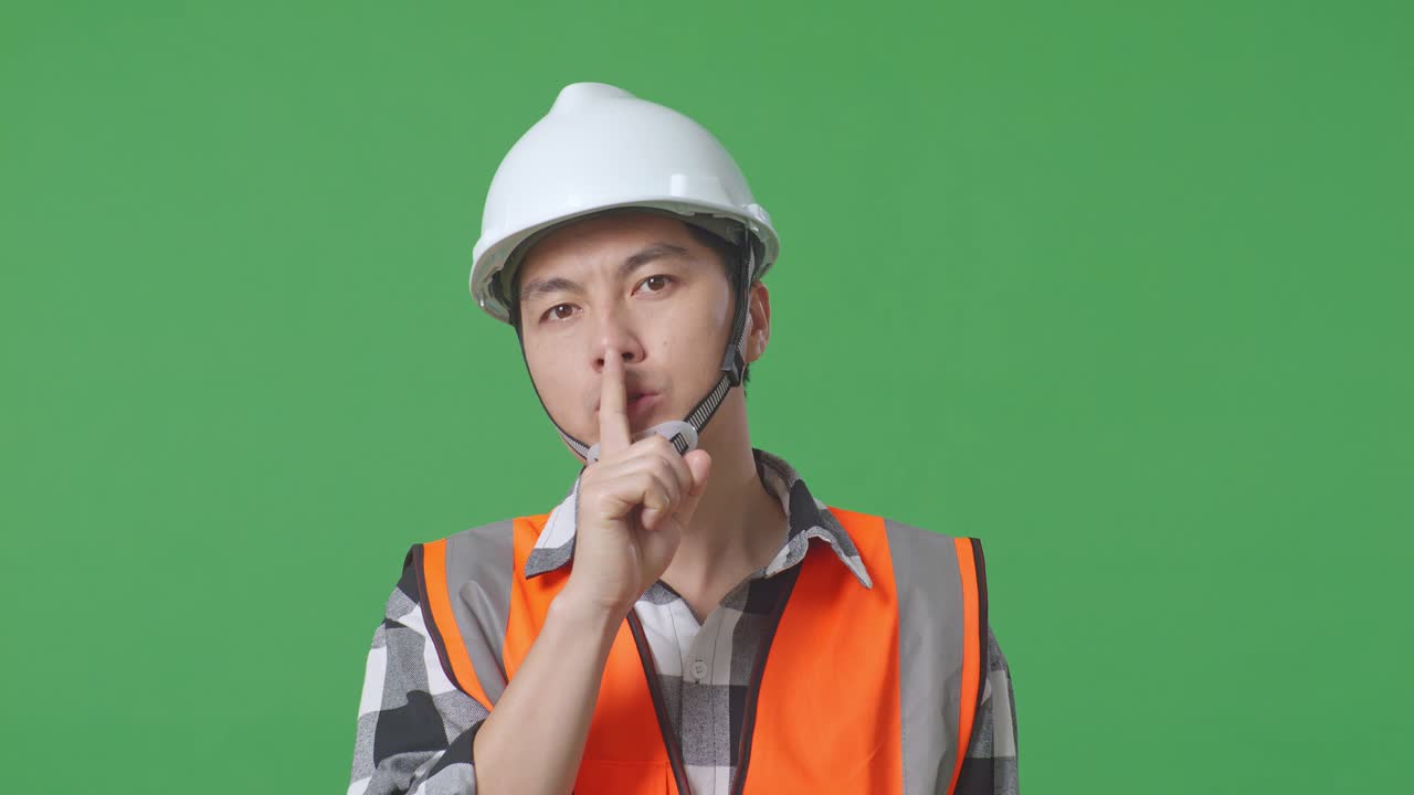 Close Up Of Asian Male Engineer With Safety Helmet Making Shh Gesture While Standing In The Green Screen Background Studio