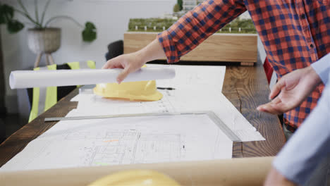 Midsection-of-diverse-male-and-female-architects-standing-at-desk-discussing-blueprints,-slow-motion