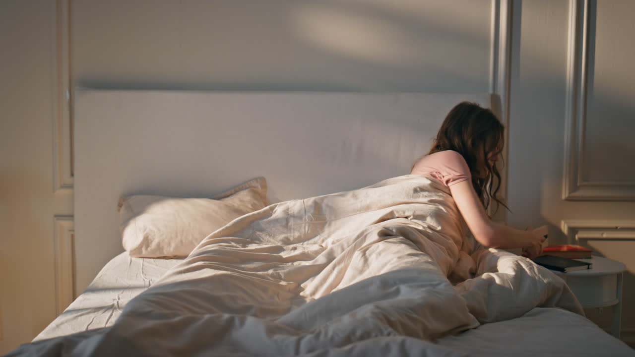 늦은 여자가 이 나는 침실에서 깨어난다. 충격에 빠진 소녀가 드폰 알람을 확인하고 있다.