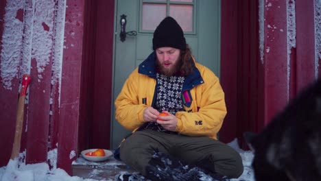 persona pelando y comiendo fruta naranja afuera con su perro durante el invierno