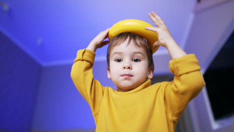 Adorable dark-haired toddler playing with pyramid ring. Baby boy putting the toy on his head. Low angle view. Close up.