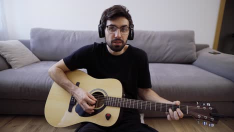 bearded man sitting on the floor, playing on guitar and looking at the camera, slow motion