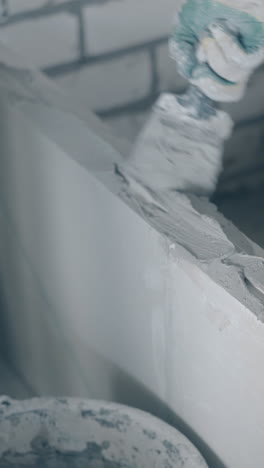 worker arm in blue sweatshirt and gloves holds putty knife and smears gypsum plasterboard wall with primer closeup