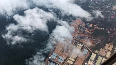 expansive aerial shot of dense malaysian forest and a developing industrial area partially covered by clouds, seen from an airplane window
