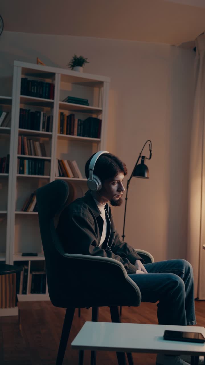 A man with headphones sits in a cozy room, illuminated by warm lighting