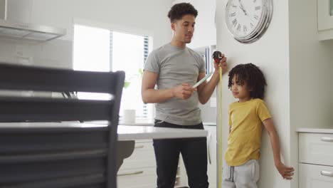 Happy-biracial-man-and-his-son-measure-height-in-kitchen